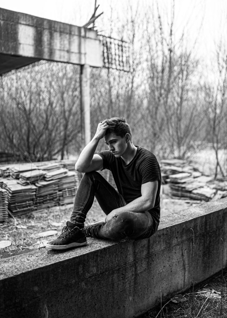 A man sits alone, deep in thought, in a monochrome urban setting.